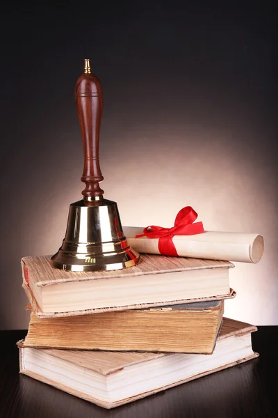 Gold retro school bell with books on table on dark background — Stock Photo, Image