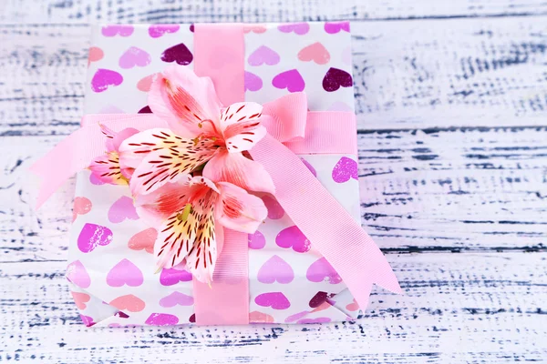 Presente rosa com arco e flor na mesa de madeira close-up — Fotografia de Stock