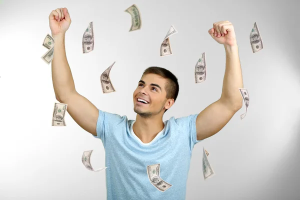Homem feliz desfrutando de chuva de dinheiro, em fundo cinza — Fotografia de Stock