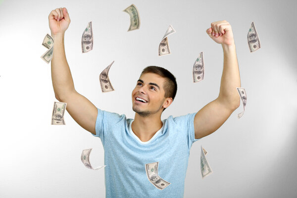 Happy man enjoying rain of money, on grey background