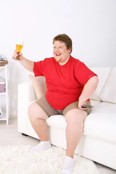 Lazy overweight male sitting with glass of beer on couch and watching television — Stock Photo, Image