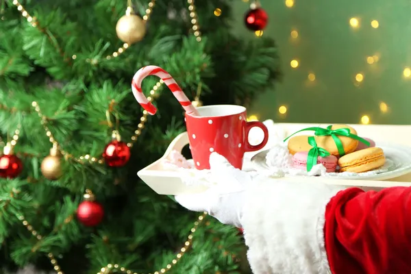 Santa håller mugg och tallrik med cookies i handen — Stockfoto