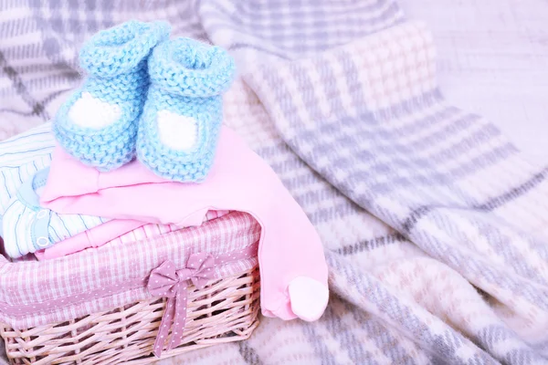 Baby clothes in basket on plaid in room — Stock Photo, Image