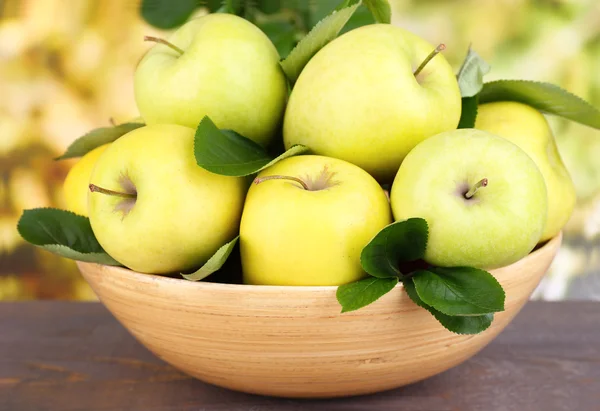 Olgun tatlı elma doğa zemin üzerine ahşap kase yaprak ile — Stok fotoğraf