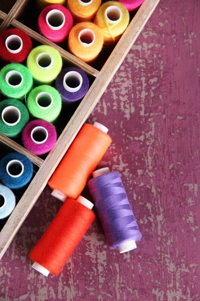 Multicolor sewing thread in wooden box, on wooden background, close-up — Stock Photo, Image