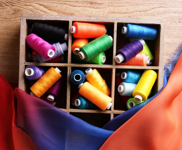 Multicolor sewing thread in wooden box, on wooden background, close-up — Stock Photo, Image