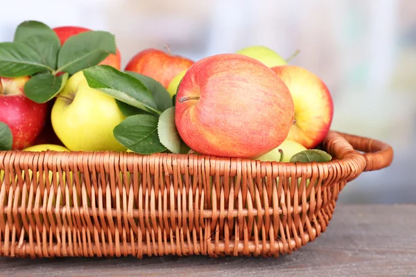 成熟的甜苹果在柳条编织的篮子在明亮的背景上的叶子 — 图库照片