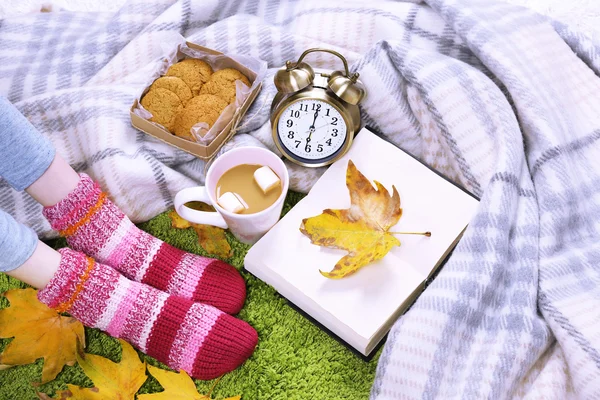 Composition avec plaid chaud, livre, tasse de boisson chaude et jambes féminines, sur fond de tapis de couleur — Photo