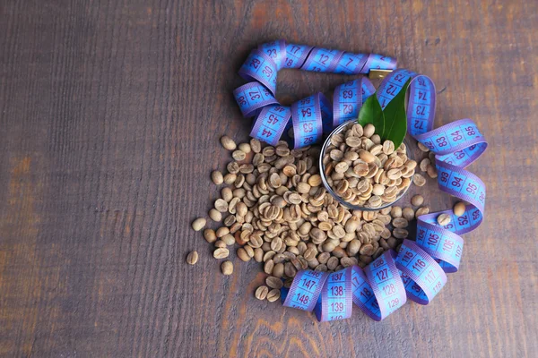 Syrové zelené kávové boby ve sklenici a měřicí pásky, na barevné dřevěné pozadí. Koncepce úbytku hmotnosti — Stock fotografie