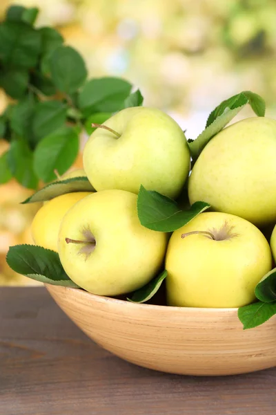 Спелые сладкие яблоки с листьями в деревянной чаше на фоне природы — стоковое фото