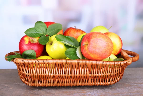 Zralé sladké jablka s listy v proutěném koši na světlé pozadí — Stock fotografie