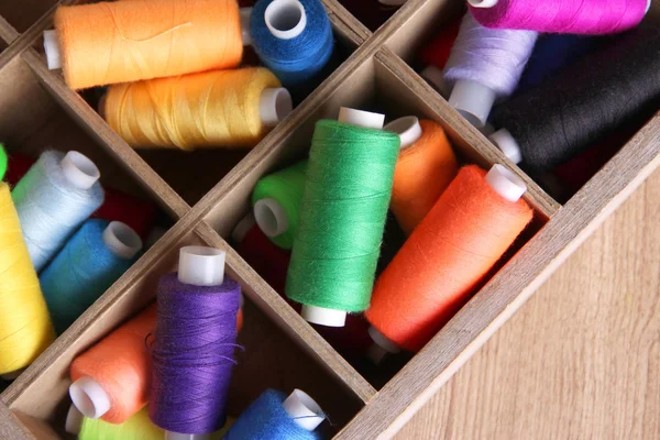 Hilo de coser multicolor en caja de madera, sobre fondo de madera, primer plano — Foto de Stock