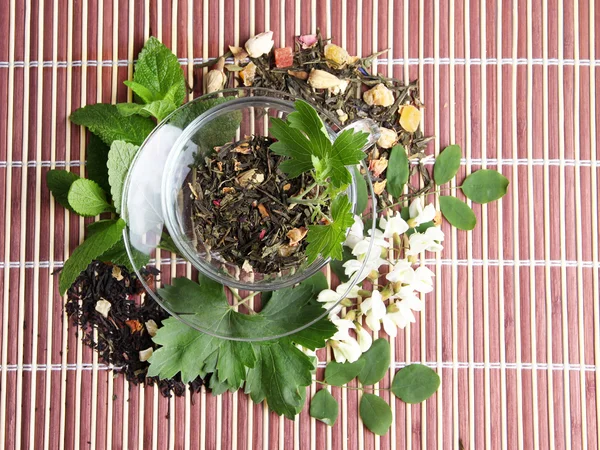 Glasschale mit trockenen Blüten und Kräuterzutaten für Tee, auf Bambusmatte Hintergrund — Stockfoto