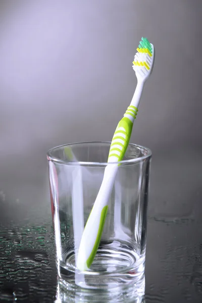 Tandenborstel in glas op grijze achtergrond — Stockfoto