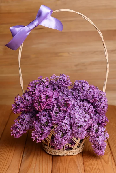 Красивые сиреневые цветы в плетеной корзине на столе на деревянном фоне — стоковое фото