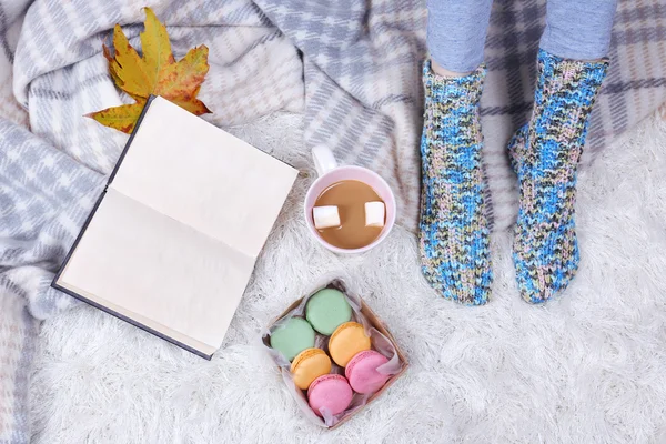 Sammansättning med varma Pläd, bok, kopp varm dryck och kvinnliga ben, på mattan färgbakgrund — Stockfoto