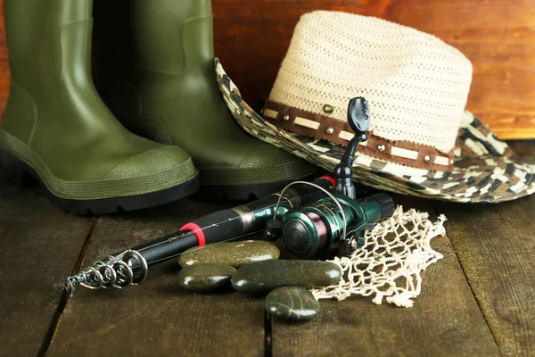 Canna da pesca, stivali di gomma e cappello sul tavolo di legno primo piano — Foto Stock