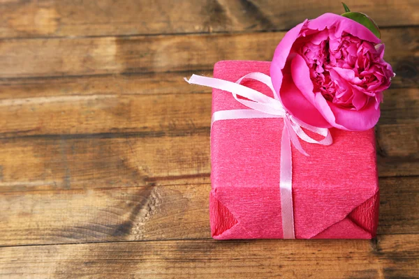 Ροζ δώρο με το τόξο και το λουλούδι στο ξύλινο τραπέζι close-up — Φωτογραφία Αρχείου