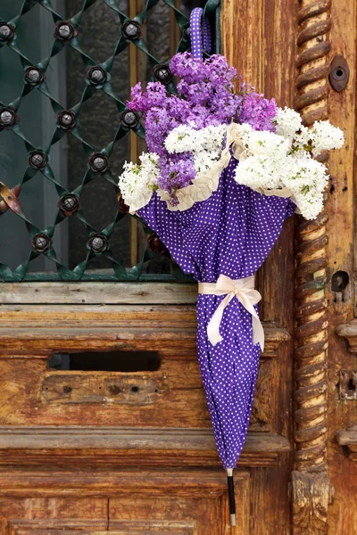 Beautiful lilac flowers in umbrella on old wooden doors — Stock Photo, Image