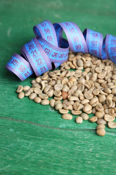 Chicchi di caffè verde crudo e metro a nastro, su sfondo di legno a colori. Concetto di perdita di peso — Foto Stock