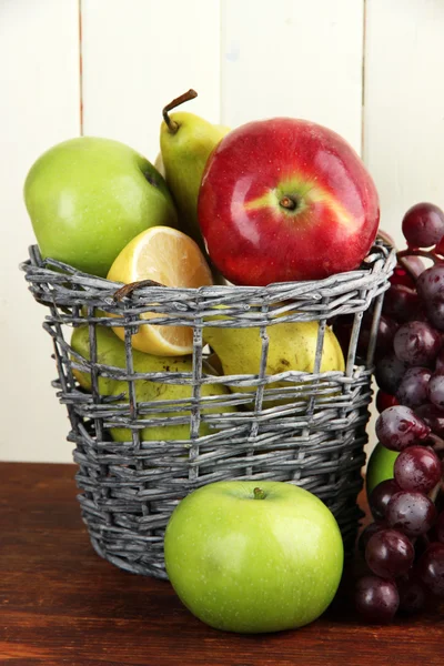 Different fruits in basket on table on wooden background — Stock Photo, Image