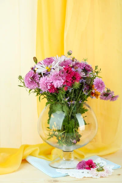 Flores silvestres en jarrón de vidrio sobre tabla sobre fondo de tela amarilla —  Fotos de Stock