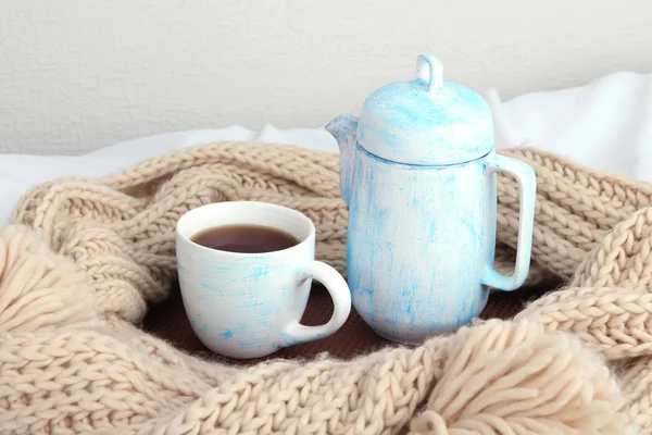 Tasse und Teekanne mit Schal auf Bett auf Wandhintergrund — Stockfoto