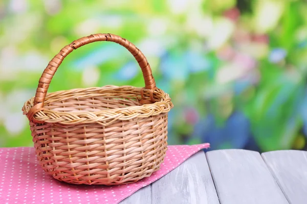 Empty wicker basket on wooden table, on bright background — Stock Photo, Image