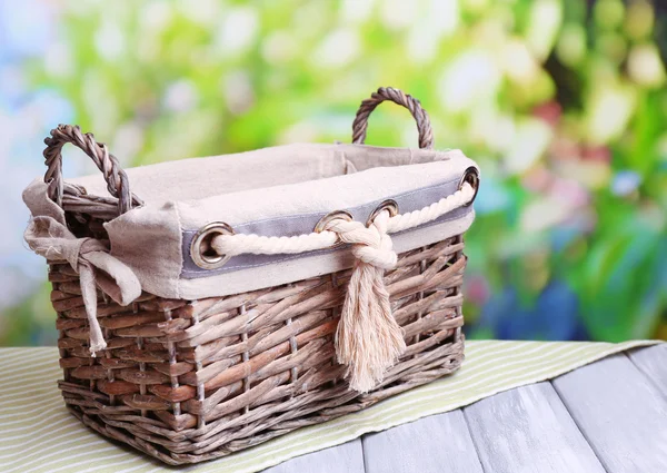 Empty wicker basket on wooden table, on bright background — Stock Photo, Image