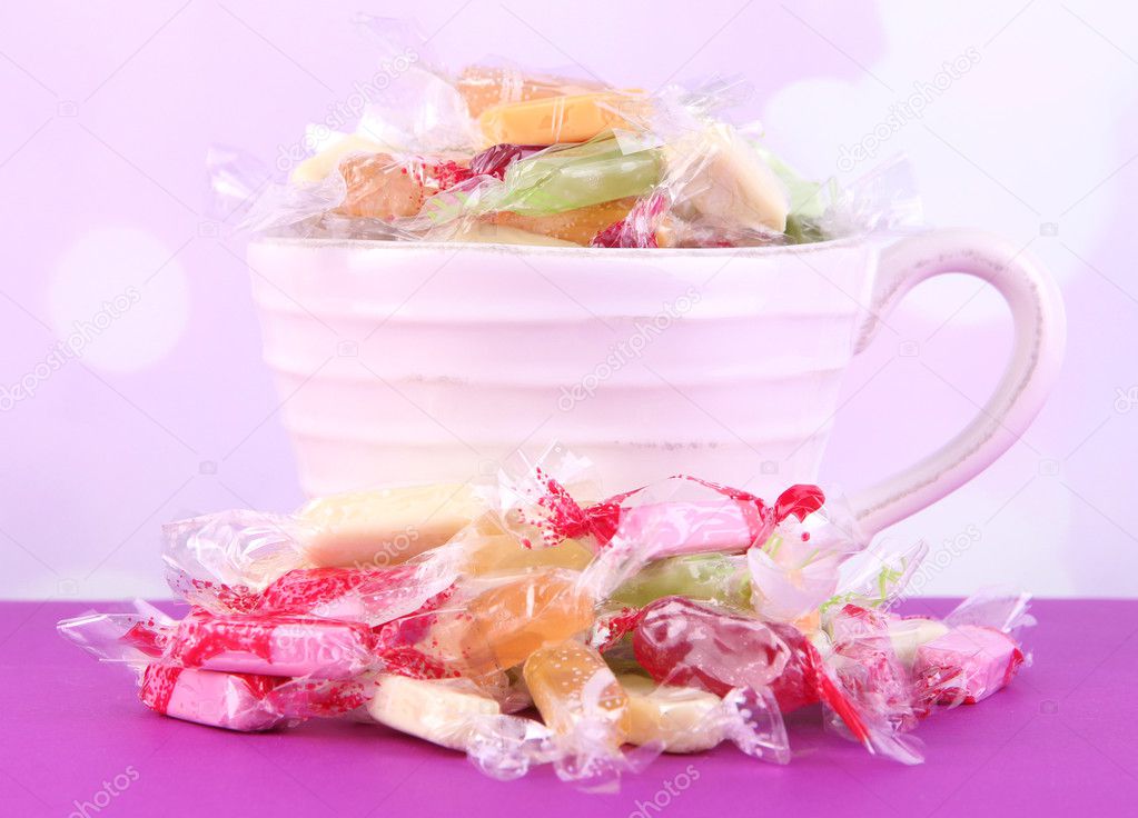 Tasty candies in mug on table on bright background