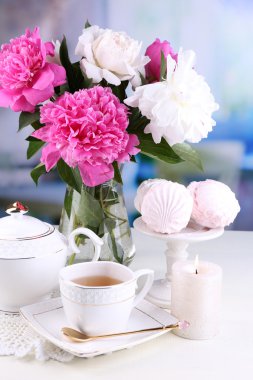 Cam vazo içinde sunulan güzel peonies, çay Kupası ve hatmi, masada açık renkli üzerinde kompozisyon