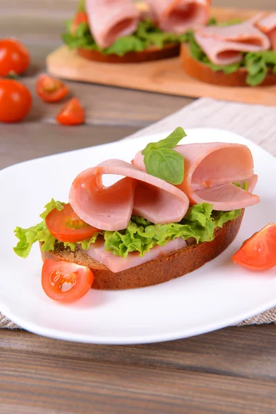 Вкусный сэндвич с салатом и ветчиной на тарелке на столе крупным планом — стоковое фото