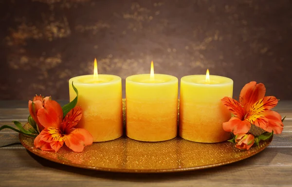 Mooie kaarsen met bloemen op tafel op bruine achtergrond — Stockfoto