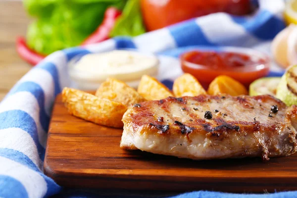 Grilovaný steak, grilovaná zelenina a smažené bramborové kousky na dřevěné desce na pozadí tabulky — Stock fotografie