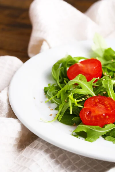 Grüner Salat mit Rucola, Tomaten und Sesam auf Teller, auf Holzgrund — Stockfoto