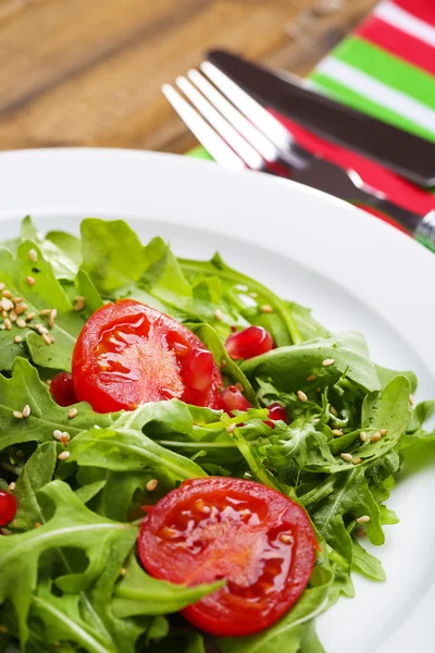 Salada verde feita com arugula, tomates e gergelim na placa, no fundo de madeira — Fotografia de Stock