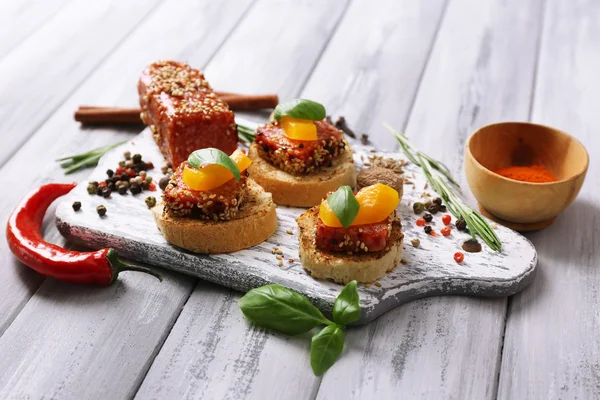 Sammansättningen av läckra smörgåsar med salami korv, basilika blad på skärbräda, på trä bakgrund — Stockfoto