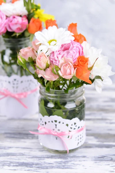 Beautiful bouquet of bright flowers in jars on table on grey background — Stock Photo, Image