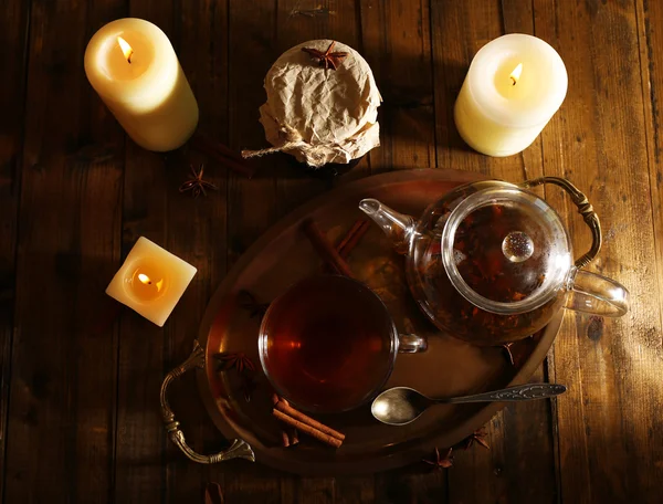 Složení s čajem v poháru a konvici a svíčky na stole, na dřevěné pozadí — Stock fotografie