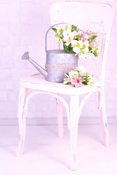 Beautiful bouquet of freesias in watering can on chair in room — Stock Photo, Image