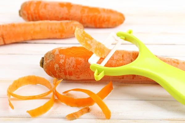 Carottes crues et éplucheur sur table en bois — Photo