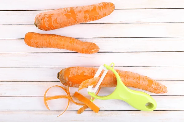 Carottes crues et éplucheur sur table en bois — Photo