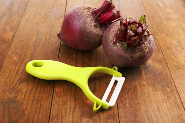 Peeler and beet on wooden table — Stock Photo, Image