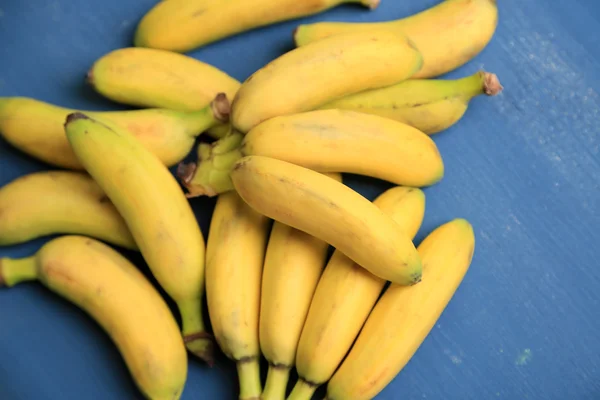 Haufen Mini-Bananen auf farbigem Holzhintergrund — Stockfoto