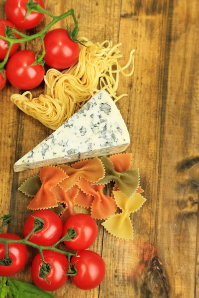 Different pasta, cheese and tomatoes on wooden table close-up — Stock Photo, Image