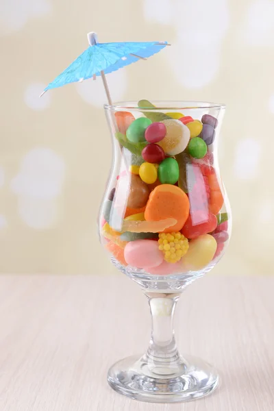 Διαφορετικά πολύχρωμα φρούτα καραμέλα σε ποτήρι στο τραπέζι επάνω ελαφρύς υπόβαθρο — Φωτογραφία Αρχείου