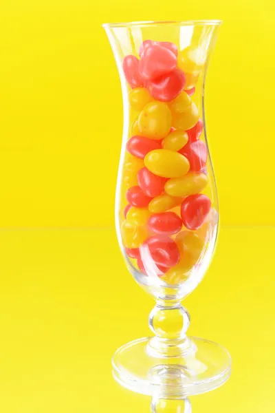 Verschiedene bunte Fruchtbonbons im Glas auf gelbem Hintergrund — Stockfoto