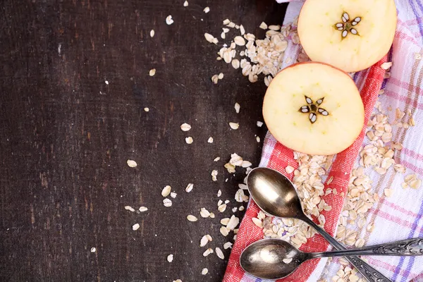 Mela con farina d'avena e cucchiai vintage su tovagliolo, su sfondo di legno a colori — Foto Stock