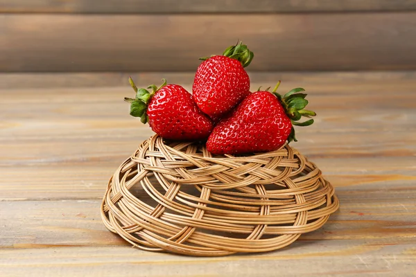 Červené zralé jahody v proutěném koši na dřevěné pozadí — Stock fotografie