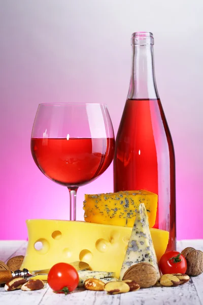 Pink wine and different kinds of cheese on colorful background — Stock Photo, Image